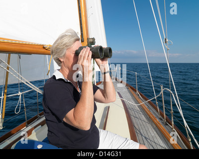 Femme plus âgée à l'aide de jumelles sur voilier Banque D'Images
