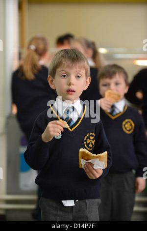 Un écolier eating toast après matin Assemblée générale à Notre Dame et St Werburgh's Catholic Primary School à Newcastle-under-Lyme, St Banque D'Images