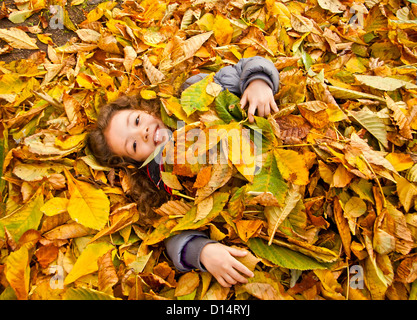 Petite fille portant sur un tas de feuilles jaunes Banque D'Images