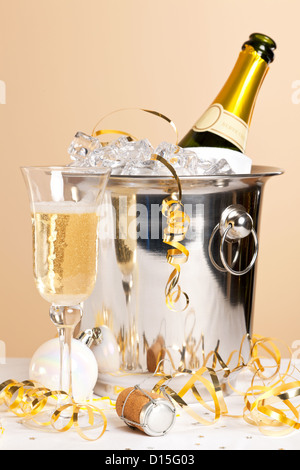 Un verre de champagne avec une bouteille dans un seau à glace et banderoles d'or à travers la table Banque D'Images