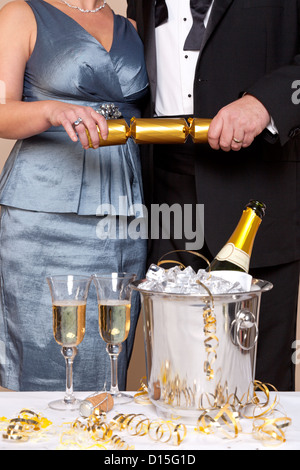 Un couple en tenue de soirée tirant une gold Christmas Cracker at un Champagne partie. Banque D'Images