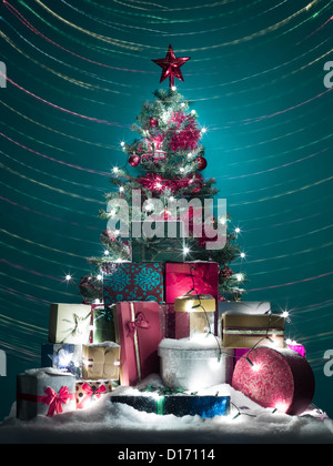 Arbre de Noël joliment décoré avec des globes rouges, tinsels et star avec une pile de shiny présente en face d'elle couverte de neige, entouré de lumières colorées Banque D'Images