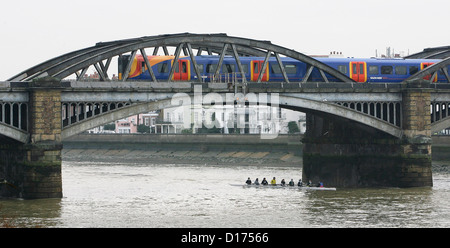 Un train passe au sud-ouest du pont Barnes dans l'ouest de Londres au-dessus un groupe de rameurs sur la Tamise. Banque D'Images