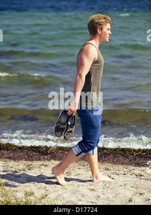 Bel homme transportant ses chaussures et marcher seule sur la plage Banque D'Images