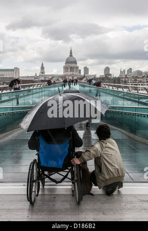 Sans-abri en fauteuil roulant assis sous la pluie avec un ami sur un pont du millenium londres Banque D'Images