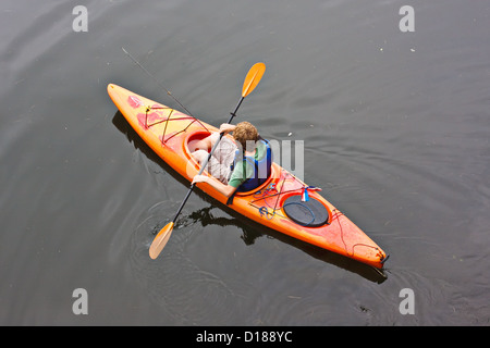 Un adolescent a une balade en kayak sur le lac. Il y a une canne à pêche dans le kayak avec lui. Banque D'Images