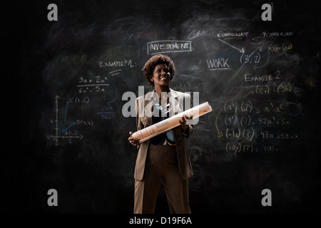 Businesswoman holding blueprint par blackboard Banque D'Images