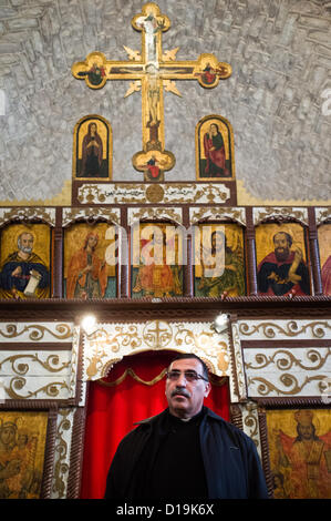 Père Nadim Shakur présente les Mi'ilya Église de l'annonciation interior showing the 'Les Filles du Calvaire", un écran couvert décoré avec des icônes et des peintures, qui sépare le hall et le sanctuaire derrière elle. Mi'ilya, Israël. 11-Dec-2012. Mi'ilya, un village arabe en Galilée occidentale, a une population de 3 100 chrétiens Melkite appartenant à l'Église catholique grecque de retrouver leurs histoire au 1er siècle les chrétiens d'Antioche, en Turquie, où le christianisme a été introduit par saint Pierre. Banque D'Images