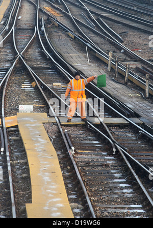 Un employé des chemins de fer qui travaillent sur la voie ferrée à Clapham Junction Gare à Londres vagues un drapeau vert. Banque D'Images