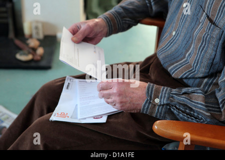 Détail d'un homme âgé assis dans fauteuil lecture / holding bill ou lettre officielle, Suffolk, Angleterre, RU Banque D'Images