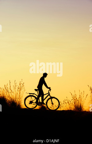 Indian boy riding bicycle parmi les graminées au coucher du soleil. Silhouette. L'Inde Banque D'Images