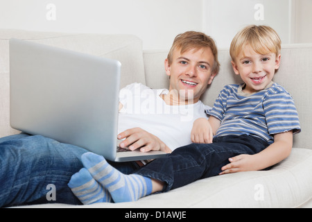 Portrait père happy boy using laptop on sofa Banque D'Images