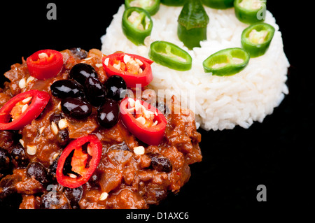 Sex et épicé Chili con Carne garni de poivrons rouges et riz au poivre vert. Sur noir Banque D'Images