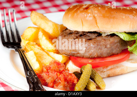 Home made simple hamburger de base avec les tranches de tomate, laitue et l'oignon dans un petit pain de pain blanc avec des croustilles et des cornichons. Banque D'Images