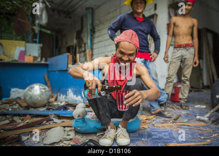 Le 12 décembre 2012 - Bangkok, Thaïlande - les travailleurs du chantier de démolition se détendre et partager une bouteille de spiritueux thaïlandais pendant qu'ils boivent à la fin de leur quart de travail dans ''Washington Square'' un célèbre quartier des divertissements de Sukhumvit Soi 22 à Bangkok. Les travailleurs du chantier de démolition sur de nombreux projets en Thaïlande en direct sur leur site d'abattre l'édifice et de recyclage que peut-recyclés comme ils le font jusqu'à ce que le site n'est plus habitable. Ils dorment sur les étages des bâtiments ou parfois dans des tentes, la cuisson au gaz ou des réchauds à charbon travaillant du matin au soir. Parfois les familles vivent et travaillent ensemble, d'autres fois Banque D'Images