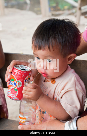 Jeune garçon de la minorité Kayan boire un verre rouge vif, Huai Seau Tao, province de Mae Hong Son, Thaïlande Banque D'Images