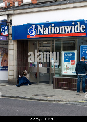 Femme sans-abri mendier dans la rue en dehors d'une agence de la banque et de laisser Banque D'Images