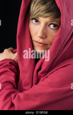 Belle mais triste jeune femme en cape rouge tenue main sur l'épaule et réfléchie à la de l'appareil photo. Portrait, Studio shot Banque D'Images