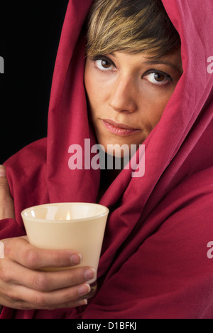 Belle mais triste jeune femme en cape rouge tenant une bougie allumée dans ses mains et réfléchi à l'appareil photo. Banque D'Images