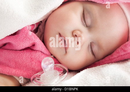 Fille bébé dort dans des serviettes en coton blanc et rose avec une sucette à proximité ; Banque D'Images