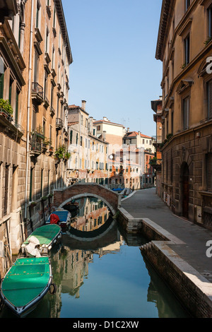 Les bateaux, les bâtiments et les ponts reflètent dans les eaux calmes d'un petit canal dans la ville de Venise Banque D'Images