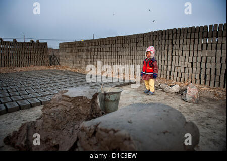 14 décembre 2012 - Bakthapur bakthapur, Népal, - un enfant se distingue par l'pilled bricks pendant que ses parents font des briques..Au Népal il y a environ 750 usines de briques, alors que seulement 450 sont enregistrés auprès du gouvernement. Il y a 110 usines de briques dans la vallée de Katmandou alors que 64 dans le district de Bakthapur. Aucune des usines répondent aux normes de l'Industrie Ministère de l'environnement de travail pour la sécurité..500 enfants travaillent dans les fours à briques 52 pour cent d'entre eux ont moins de 10 ans. Embauche de travailleurs saisonniers des fours d'autres districts par intermédiaire qui bénéficiez d'un montant de gains du travailleur..Par la fabrication de briques, de travail Banque D'Images