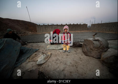 14 décembre 2012 - Bakthapur bakthapur,, Népal - Kumari Manandhar (19) faire des briques alors que son enfant est âgé d'un an par le mur de briques à Bakthapur. Les enfants de brique travailleurs demeurent souvent sans surveillance lorsque les deux travaillent..Au Népal il y a environ 750 usines de briques, alors que seulement 450 sont enregistrés auprès du gouvernement. Il y a 110 usines de briques dans la vallée de Katmandou alors que 64 dans le district de Bakthapur. Aucune des usines répondent aux normes de l'Industrie Ministère de l'environnement de travail pour la sécurité..500 enfants travaillent dans les fours à briques 52 pour cent d'entre eux ont moins de 10 ans. Travail saisonnier location fours Banque D'Images