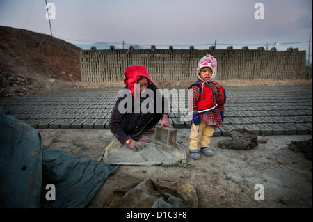 14 décembre 2012 - Bakthapur bakthapur,, Népal - Kumari Manandhar (19) faire des briques alors que son enfant est âgé d'un an par le mur de briques à Bakthapur. Les enfants de brique travailleurs demeurent souvent sans surveillance lorsque les deux travaillent..Au Népal il y a environ 750 usines de briques, alors que seulement 450 sont enregistrés auprès du gouvernement. Il y a 110 usines de briques dans la vallée de Katmandou alors que 64 dans le district de Bakthapur. Aucune des usines répondent aux normes de l'Industrie Ministère de l'environnement de travail pour la sécurité..500 enfants travaillent dans les fours à briques 52 pour cent d'entre eux ont moins de 10 ans. Travail saisonnier location fours Banque D'Images