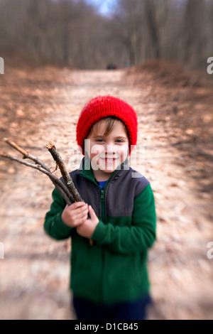 Petit garçon en molleton et red hat passe une randonnée et la collecte de bois de feu Banque D'Images