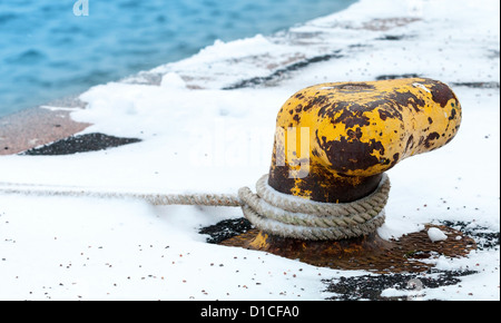 Ancien mouillage jaune rouillé bollard avec corde de marine en hiver Banque D'Images