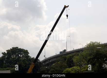 Le levage des machines à côté d'un pont aérien à Singapour. Il y a des véhicules sur le pont et verdure en dessous. Banque D'Images