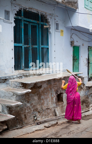 Femme indienne en sari balayant les étapes devant son domicile à Udaipur Banque D'Images