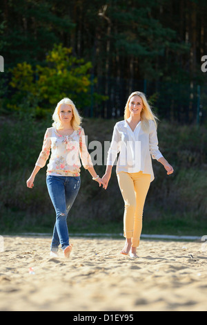 Deux jeunes femmes blonde heureuse marche main dans la main on sandy beach Banque D'Images