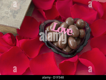 Les pétales et les amandes au chocolat dans un plat en forme de coeur Banque D'Images