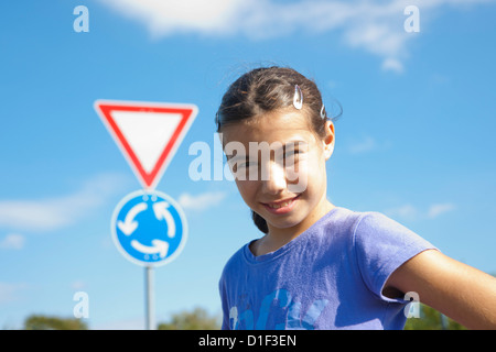 Smiling Girl standing in front of traffic sign, portrait Banque D'Images