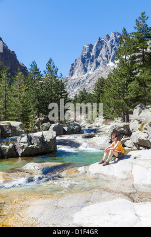 Femme assise au bord de la rivière de la Restonica, Corse, France Banque D'Images