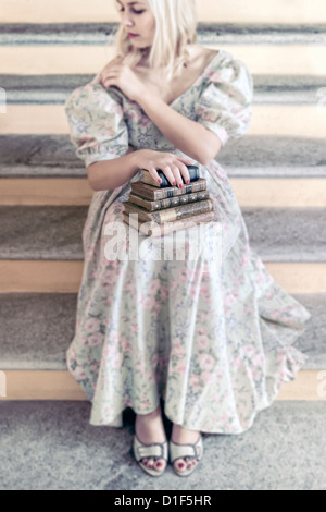 Une femme dans une robe florale tient une pile de livres anciens sur ses genoux Banque D'Images