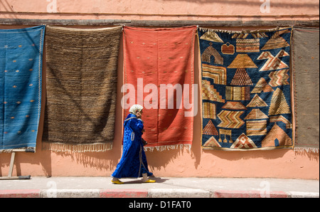 Une femme en robe islamique marcher par un mur décoré de tapis dans la médina de Marrakech, Maroc, Afrique du Nord, Afrique Banque D'Images