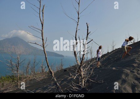 Torched arbres avec l'île de Rakata en arrière-plan pendant que deux touristes négocier la pente abrupte de Krakatau ; l'Ouest de Java. Banque D'Images