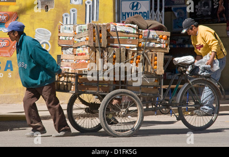 Man pulling panier chargé avec des caisses de mandarines le long d'une rue à Puno, Pérou Amérique du Sud Banque D'Images