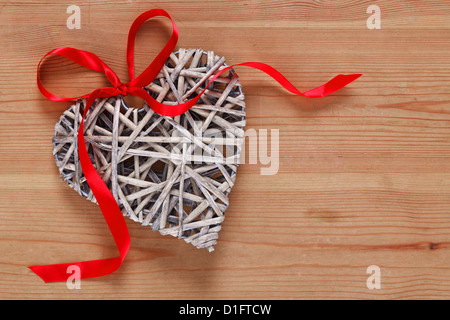 Une décoration en osier en forme de coeur avec ruban rouge sur un fond de bois rustique. Banque D'Images