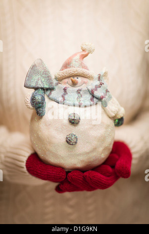 Femme portant un chandail et des mitaines rouges saisonniers titulaires d'un Bonhomme de neige en verre décoré. Banque D'Images