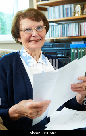 Senior woman at home with utility bills looking at camera and smiling Banque D'Images