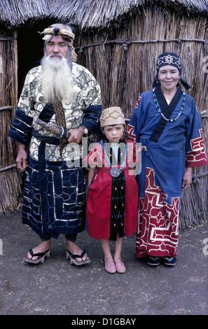 Un couple d'Ainu et leur petite-fille en robe traditionnelle posent en 1962 à l'extérieur de leur roseau et se précipite à la maison sur l'île d'Hokkaido dans le nord du Japon. Banque D'Images