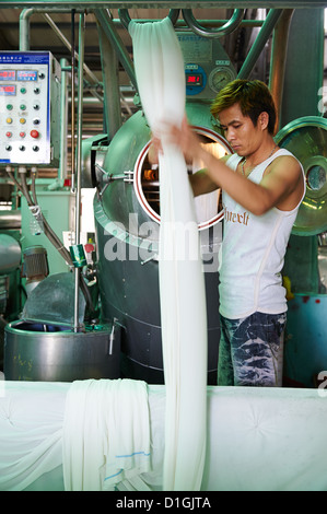 Un travailleur solide tissu et inspecte les pose à côté de grandes machines de mourir à un fabricant de textiles Banque D'Images