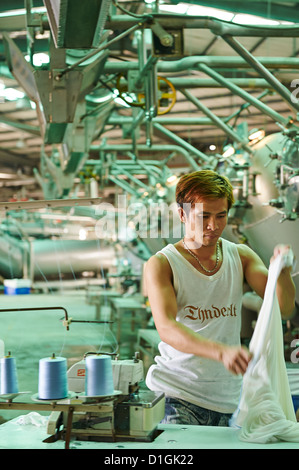 Un travailleur solide tissu et inspecte les pose à côté de grandes machines de mourir à un fabricant de textiles Banque D'Images