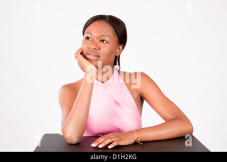 Jolie femme noire dans une robe rose, avec sa main à son menton et à la recherche de façon réfléchie dans une expression pensive Banque D'Images