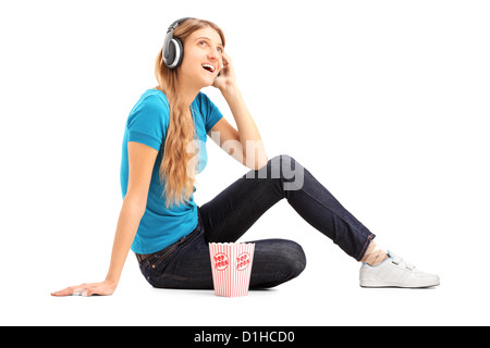 Femme blonde à l'écoute une musique et eating popcorn isolé sur fond blanc Banque D'Images