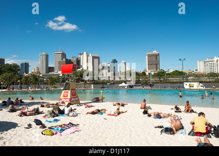 South Bank Artificial Beach Brisbane Australie | BRISBANE, Australie — les bains de soleil couvrent le sable de South Bank's Streets Beach, un lagon de baignade chloré construit sur l'ancien site de l'exposition universelle de 88, directement en face de la Brisbane River, à partir du quartier central des affaires. Le lagon artificiel a été la première plage artificielle du centre-ville d'Australie, dans le cadre d'un réaménagement qui a transformé cette zone industrielle au bord de la rivière en parc public permanent. Une tour de sauveteurs surveille les nageurs face à la ligne d'horizon du centre-ville. Banque D'Images