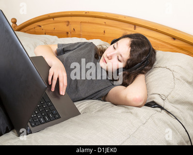 Jeune fille dans le lit de repos lors de la navigation sur internet sur son ordinateur portable Banque D'Images